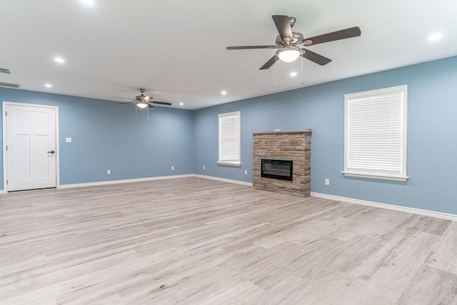 unfurnished living room featuring light hardwood / wood-style flooring, a stone fireplace, and ceiling fan