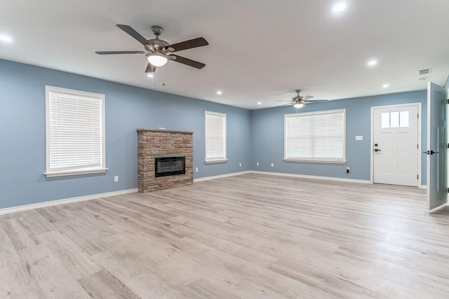 unfurnished living room with a stone fireplace, ceiling fan, and light wood-type flooring