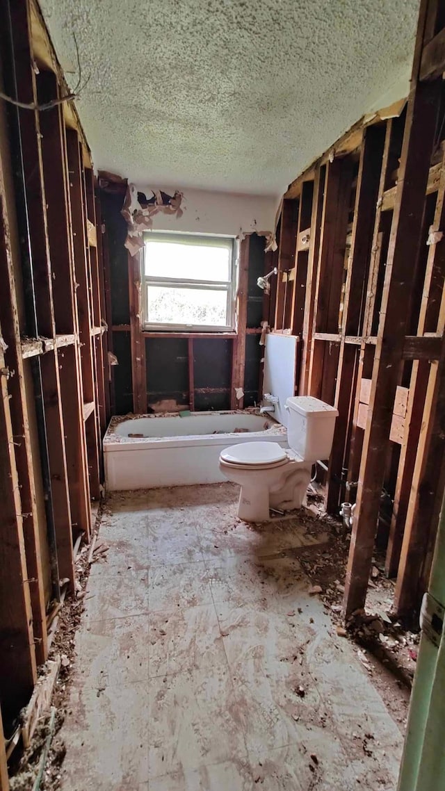 bathroom with a textured ceiling, toilet, and a bathing tub