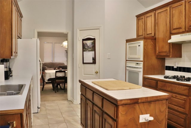 kitchen featuring tasteful backsplash, white appliances, light tile patterned floors, tile countertops, and a center island