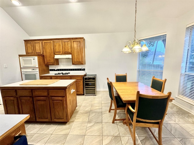 kitchen featuring lofted ceiling, beverage cooler, white appliances, and decorative light fixtures