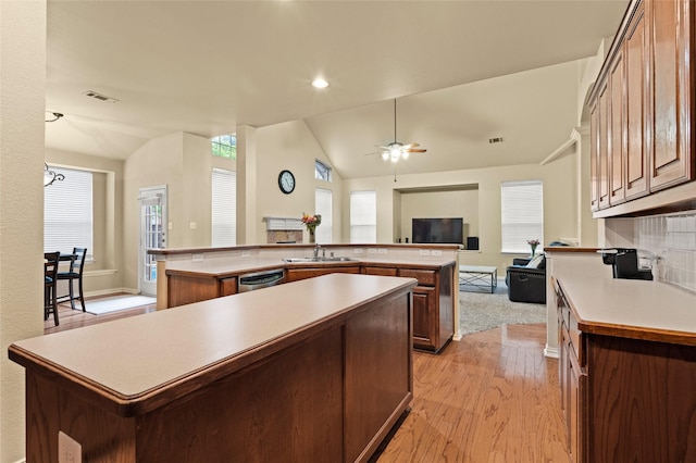 kitchen featuring lofted ceiling, a center island, decorative backsplash, sink, and light wood-type flooring