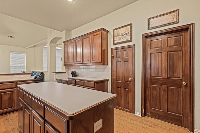 kitchen featuring decorative columns, light hardwood / wood-style flooring, tasteful backsplash, and a kitchen island