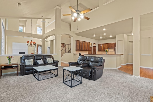 carpeted living room featuring ceiling fan with notable chandelier, a high ceiling, and ornate columns