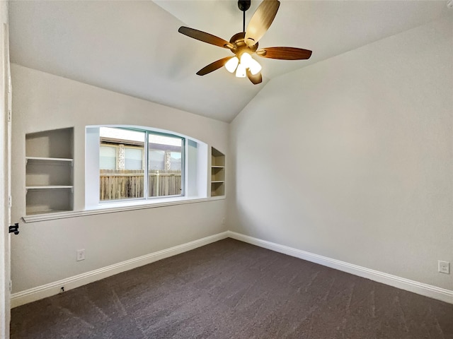 spare room featuring ceiling fan, dark carpet, built in features, and vaulted ceiling