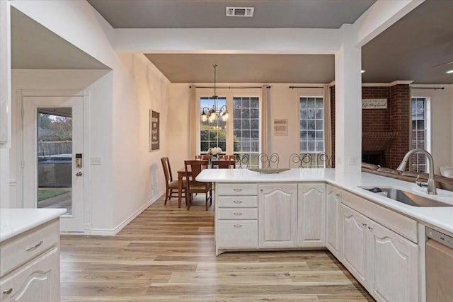 kitchen with dishwasher, sink, an inviting chandelier, light hardwood / wood-style flooring, and pendant lighting