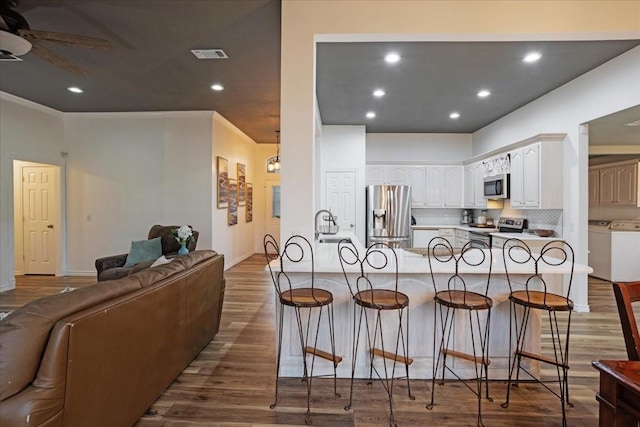 kitchen featuring a breakfast bar area, white cabinetry, wood-type flooring, and appliances with stainless steel finishes