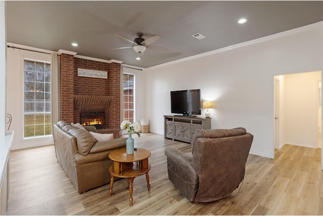 living room featuring crown molding, a fireplace, ceiling fan, and light wood-type flooring