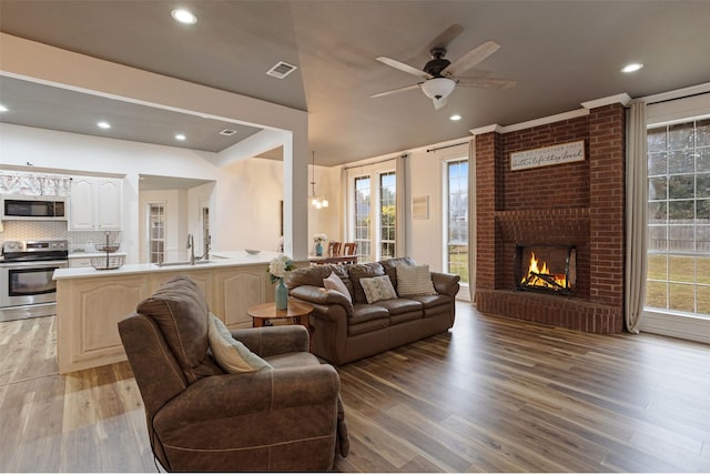 living room with light wood-type flooring, a brick fireplace, ceiling fan, and sink