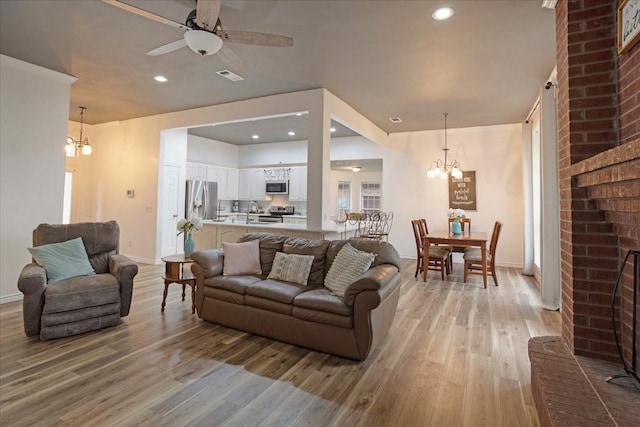 living room featuring ceiling fan with notable chandelier, light hardwood / wood-style floors, and a brick fireplace