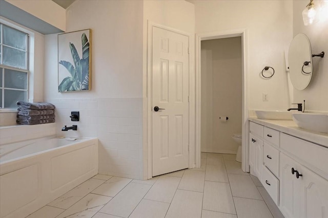 bathroom featuring vanity, a tub to relax in, toilet, and tile walls