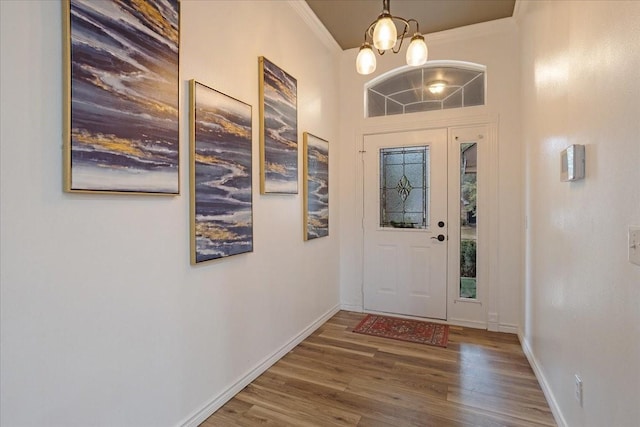 foyer entrance with hardwood / wood-style floors, crown molding, and an inviting chandelier