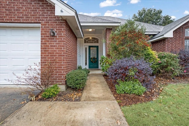 view of exterior entry featuring an attached garage, brick siding, and roof with shingles