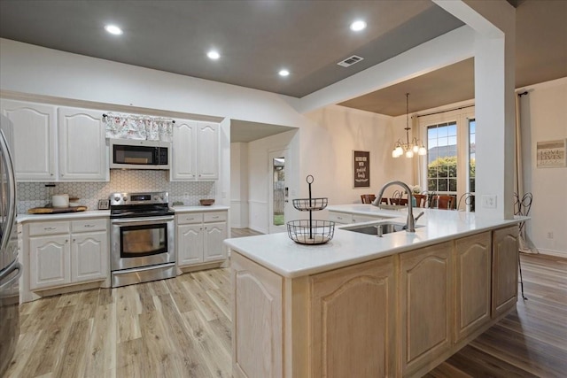 kitchen featuring stainless steel appliances, sink, pendant lighting, light hardwood / wood-style flooring, and an island with sink