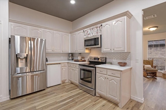 kitchen with white cabinets, light hardwood / wood-style floors, backsplash, and appliances with stainless steel finishes