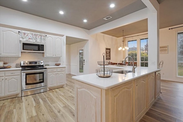 kitchen featuring appliances with stainless steel finishes, light hardwood / wood-style flooring, hanging light fixtures, and an island with sink