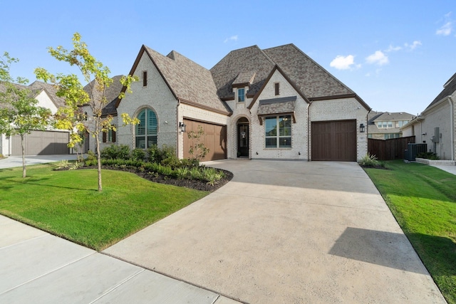 french country inspired facade with central AC unit, a garage, and a front yard