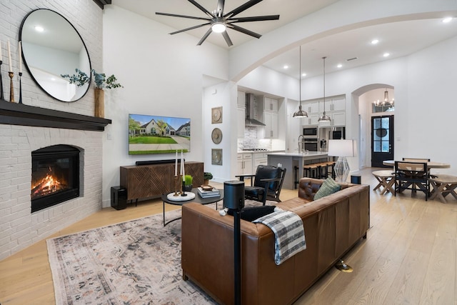 living room featuring ceiling fan with notable chandelier, light wood-type flooring, and a brick fireplace