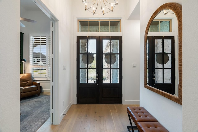 entryway with light hardwood / wood-style floors, an inviting chandelier, and french doors