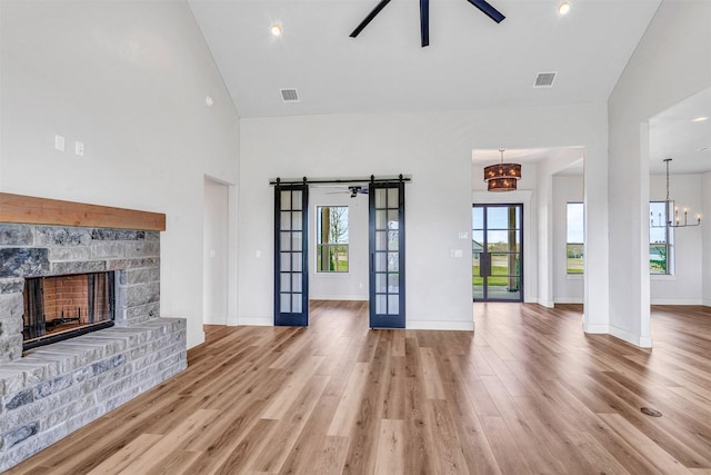 unfurnished living room featuring french doors, ceiling fan with notable chandelier, hardwood / wood-style flooring, and a stone fireplace