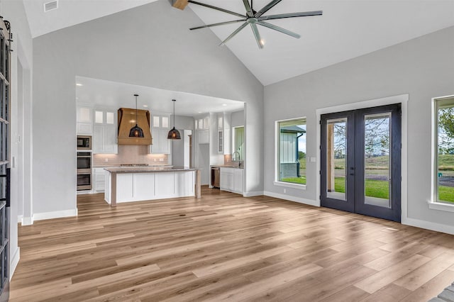 unfurnished living room featuring high vaulted ceiling, french doors, sink, light hardwood / wood-style flooring, and a barn door