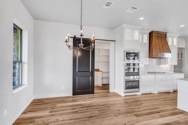 kitchen with white cabinets, light wood-type flooring, appliances with stainless steel finishes, a notable chandelier, and custom range hood