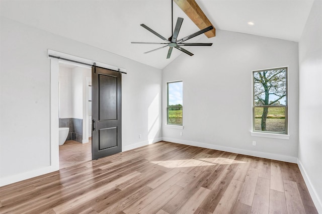 unfurnished bedroom with lofted ceiling with beams, a barn door, light wood-type flooring, and multiple windows