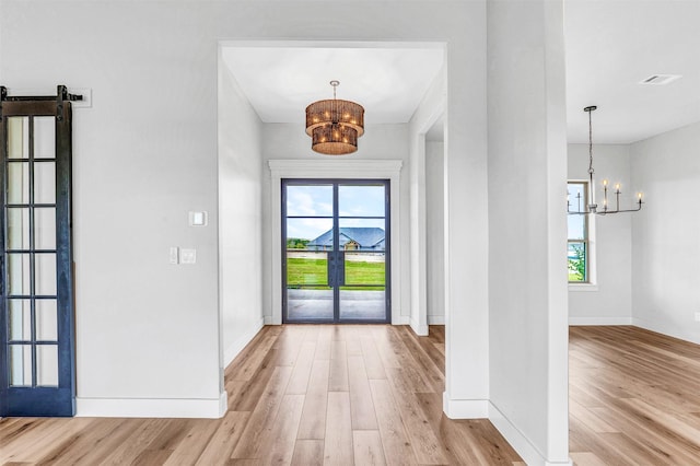 entryway with french doors, light wood-type flooring, a barn door, and a notable chandelier