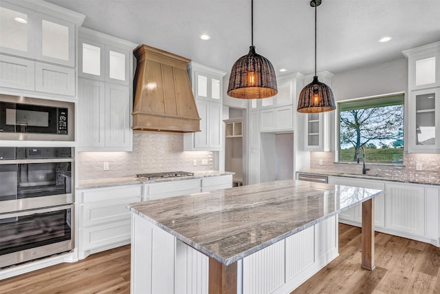 kitchen featuring custom range hood, stainless steel appliances, a kitchen island, sink, and white cabinetry