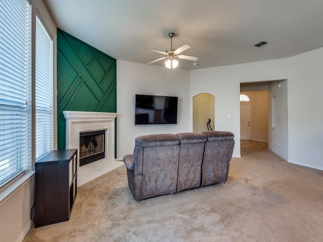 living room with a tile fireplace, ceiling fan, and light carpet