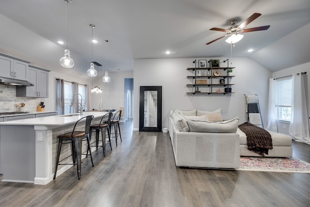 living room with ceiling fan, sink, wood-type flooring, and lofted ceiling