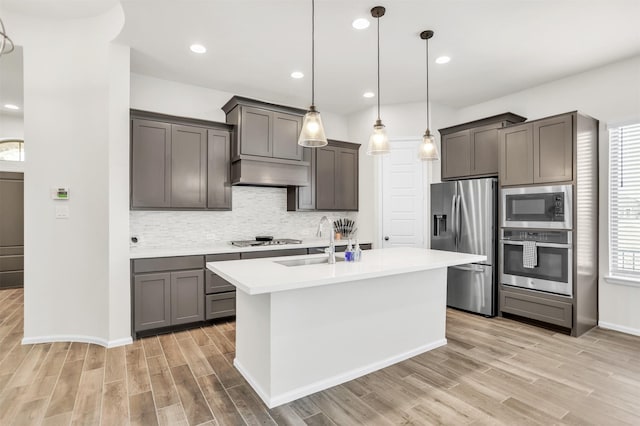 kitchen featuring appliances with stainless steel finishes, sink, pendant lighting, light hardwood / wood-style flooring, and an island with sink