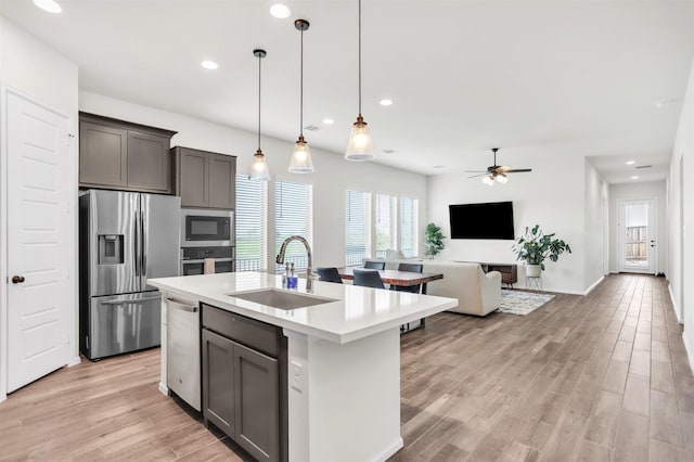 kitchen featuring sink, stainless steel appliances, light hardwood / wood-style floors, decorative light fixtures, and a center island with sink