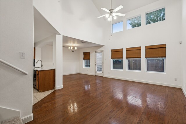 living room with ceiling fan with notable chandelier, a towering ceiling, and light hardwood / wood-style floors