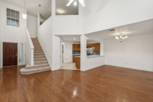 unfurnished living room featuring ceiling fan with notable chandelier, dark wood-type flooring, and a towering ceiling