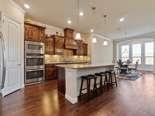 kitchen with a kitchen island with sink, dark wood-type flooring, sink, hanging light fixtures, and stainless steel appliances