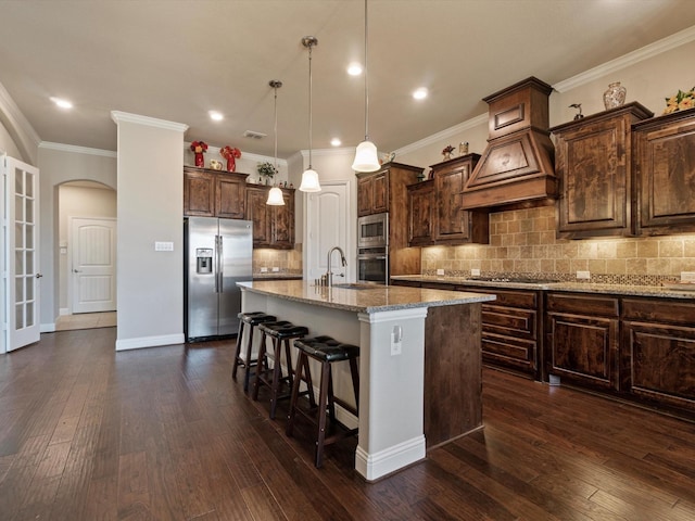 kitchen featuring light stone counters, stainless steel appliances, decorative light fixtures, a center island with sink, and dark hardwood / wood-style floors