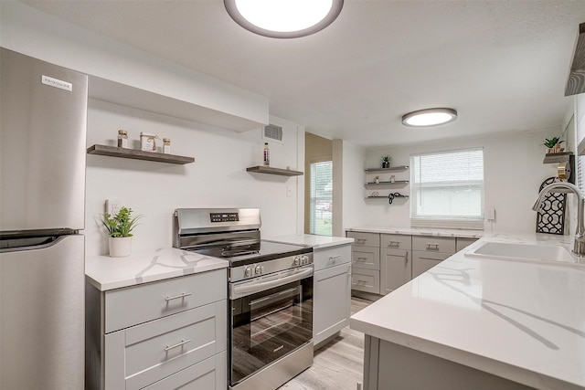 kitchen with sink, gray cabinetry, light stone counters, light hardwood / wood-style floors, and stainless steel appliances