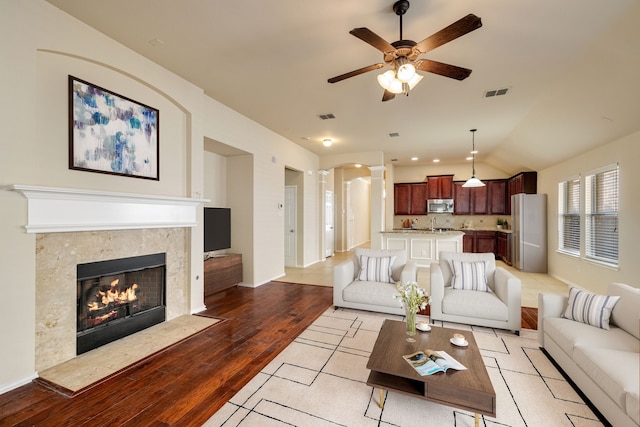 living room featuring ceiling fan, light wood-type flooring, a fireplace, and vaulted ceiling