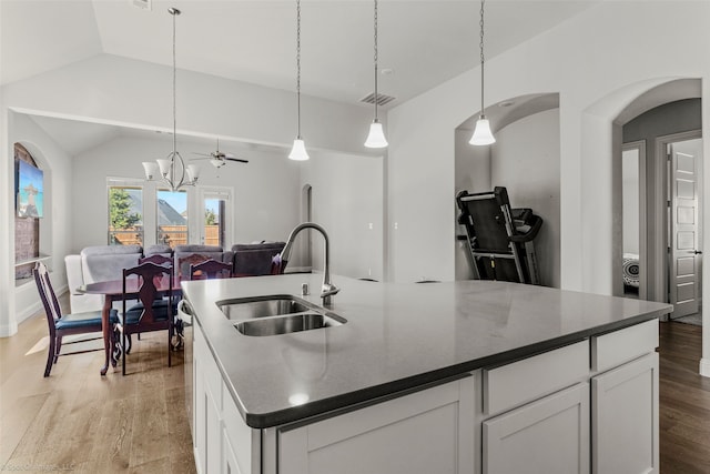 kitchen featuring sink, light hardwood / wood-style floors, vaulted ceiling, a center island with sink, and white cabinets