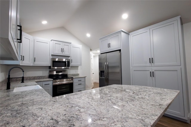 kitchen with light stone counters, stainless steel appliances, vaulted ceiling, and sink