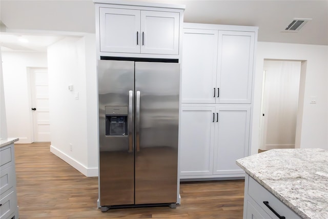 kitchen featuring light stone countertops, wood-type flooring, stainless steel fridge with ice dispenser, and white cabinets