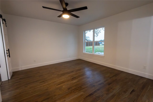 empty room featuring dark hardwood / wood-style floors, a barn door, and ceiling fan