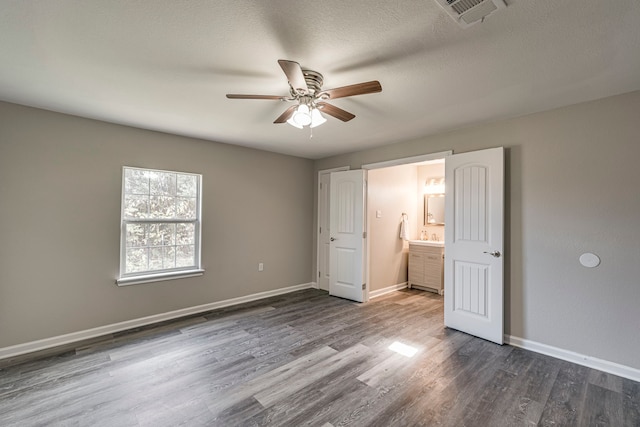 unfurnished bedroom with a textured ceiling, dark hardwood / wood-style flooring, ensuite bath, and ceiling fan