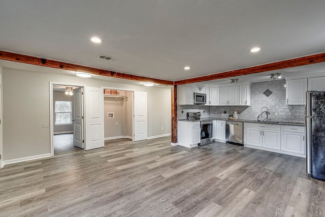 kitchen featuring white cabinets, light stone countertops, appliances with stainless steel finishes, tasteful backsplash, and light hardwood / wood-style floors