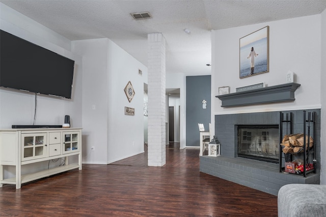 living room featuring decorative columns, dark wood-type flooring, a textured ceiling, and a fireplace