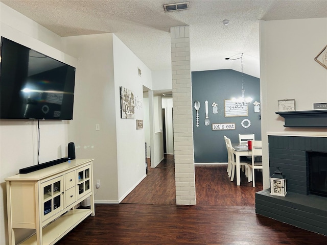 living room with vaulted ceiling, a brick fireplace, a textured ceiling, dark hardwood / wood-style floors, and decorative columns