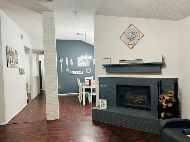 living room with a brick fireplace, a textured ceiling, dark hardwood / wood-style floors, and vaulted ceiling