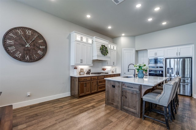 kitchen with a kitchen island with sink, dark wood-type flooring, sink, appliances with stainless steel finishes, and white cabinetry