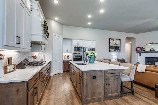 kitchen with appliances with stainless steel finishes, an island with sink, a breakfast bar area, white cabinets, and hardwood / wood-style flooring